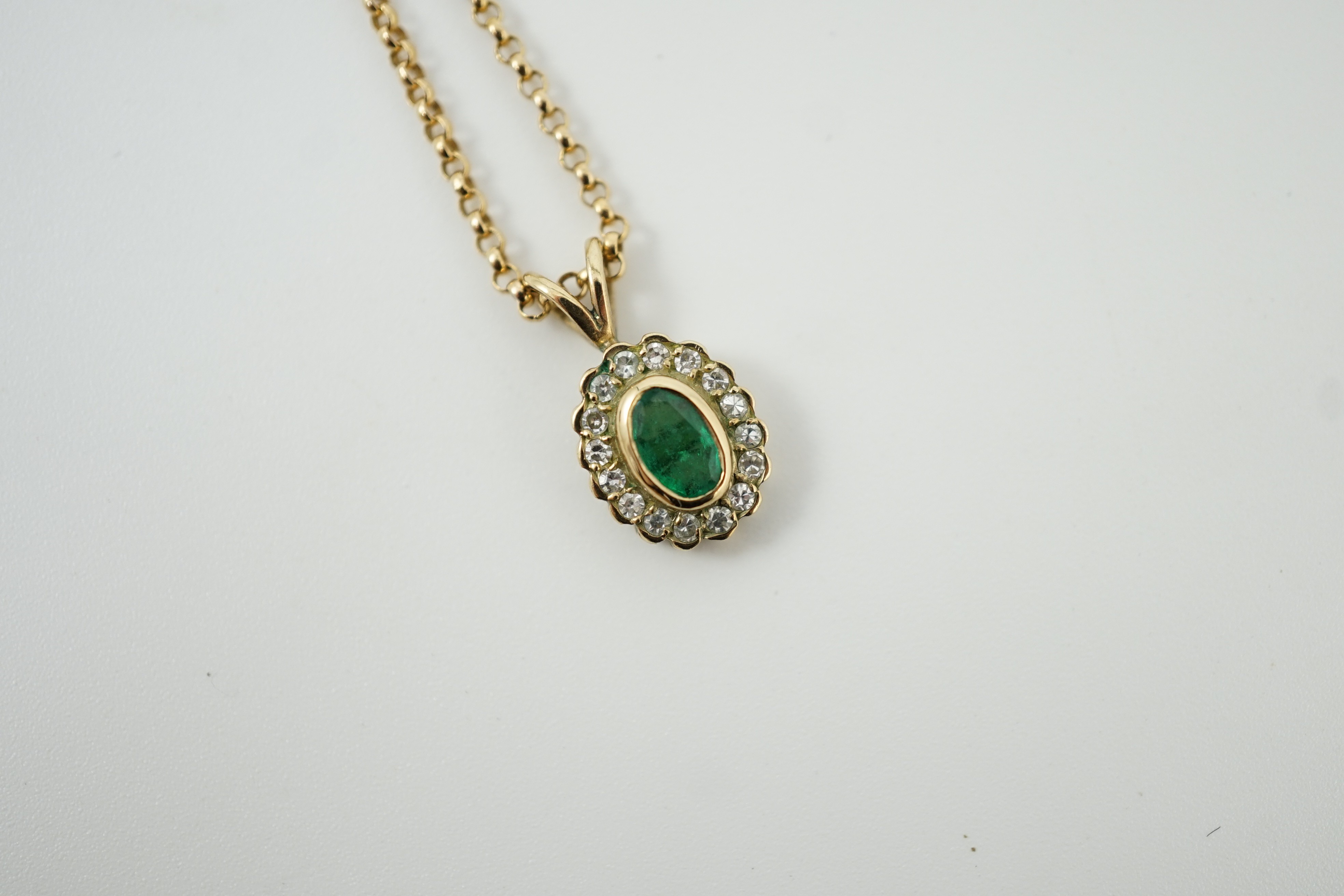 A modern 9ct gold, emerald and diamond set oval cluster pendant, 16mm, on a 9ct gold chain, 44cm, gross weight 4.1 grams.